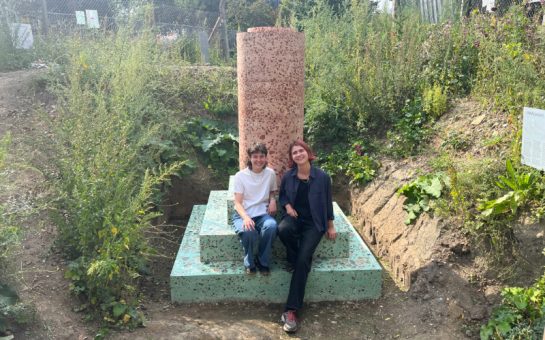 Two sculptors sit on their sculpture, which mimics a building foundation.