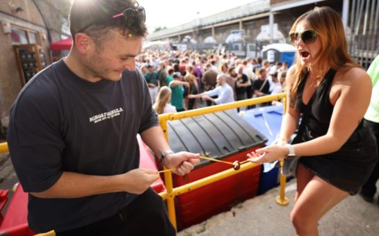 Image shows two people playing conkers with a big crowd in the background.