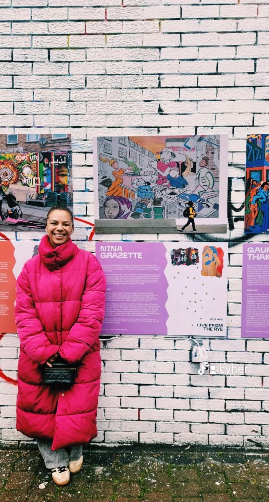 Picture of Artist standing in front of mural design displayed outside 